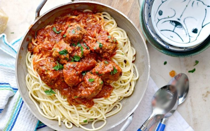A photo from above of Blow Your Mind Meatballs that shows 3 spoons, 3 bowls stacked up and a kitchen towel