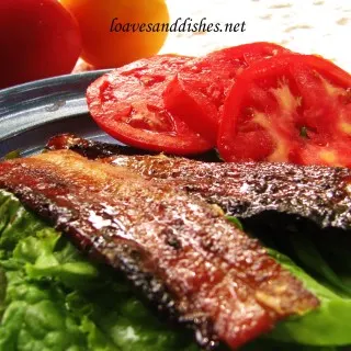 two slices of cooked bacon with tomato slices sitting on lettuce