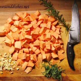 cut up sweet potatos with sprig of rosemary and garlic on cutting board