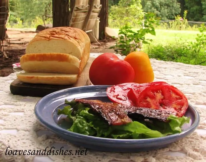 bacon on lettuce with tomato and a loaf of bread on a white table cloth