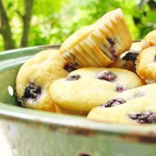 several mini blueberry muffins in a green bowl on a white table cloth