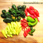 green and red peppers of varying sizes on a cutting board