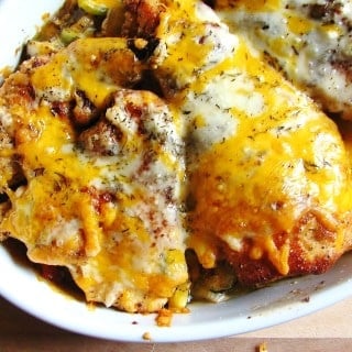 cooked chicken with melted cheese on top of veggies in white baking dish