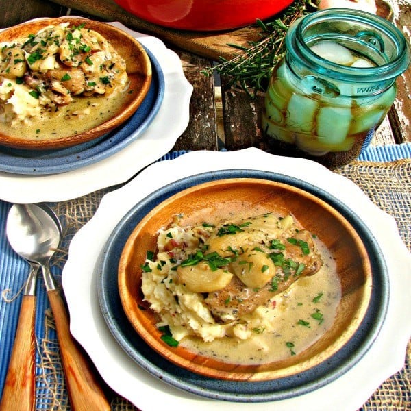 wooden plate on top of white plate with chicken thigh, sauce and garlic cloves