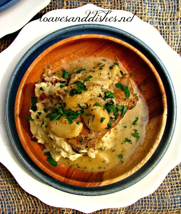 40 Garlic Chicken with mashed potatoes on a wooden plate with parsley sprinkled on top