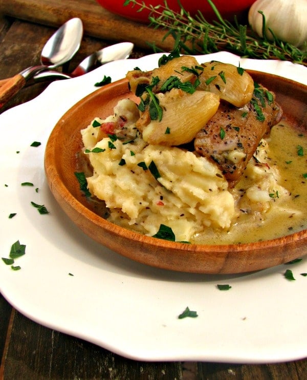 side view of mashed potatoes, creamy garlic chicken thighs on white plate with spoons