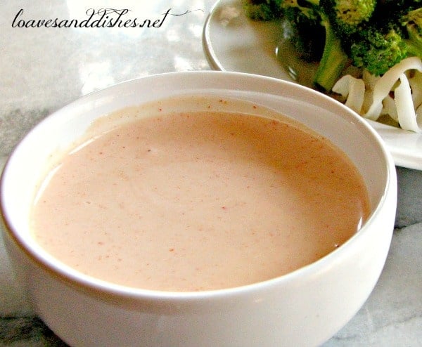 White bowl of pink shrimp sauce with broccoli in background