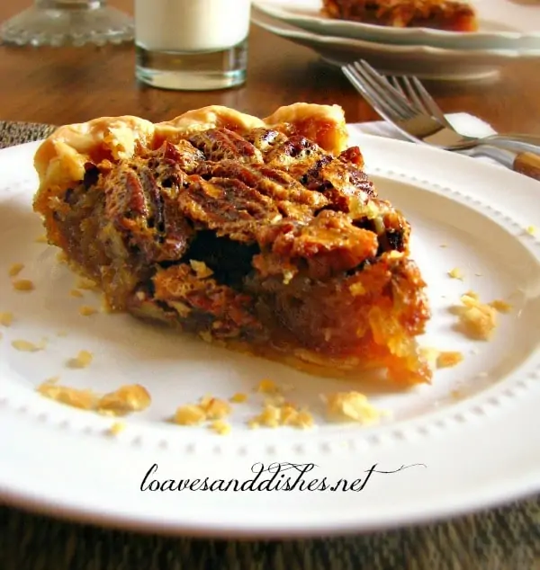 Slice of pecan pie on a white plate sitting on a wooden table