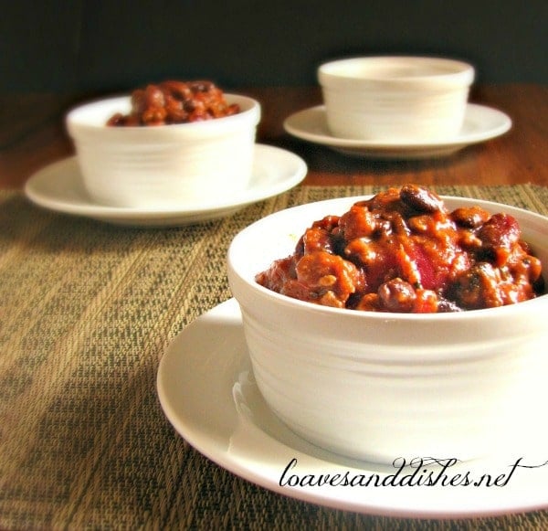 Two bowls of party chili, one in the foreground and one in the background with one empty bowl way back