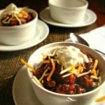 Party Chili with cheese and sour cream on top in a white bowl