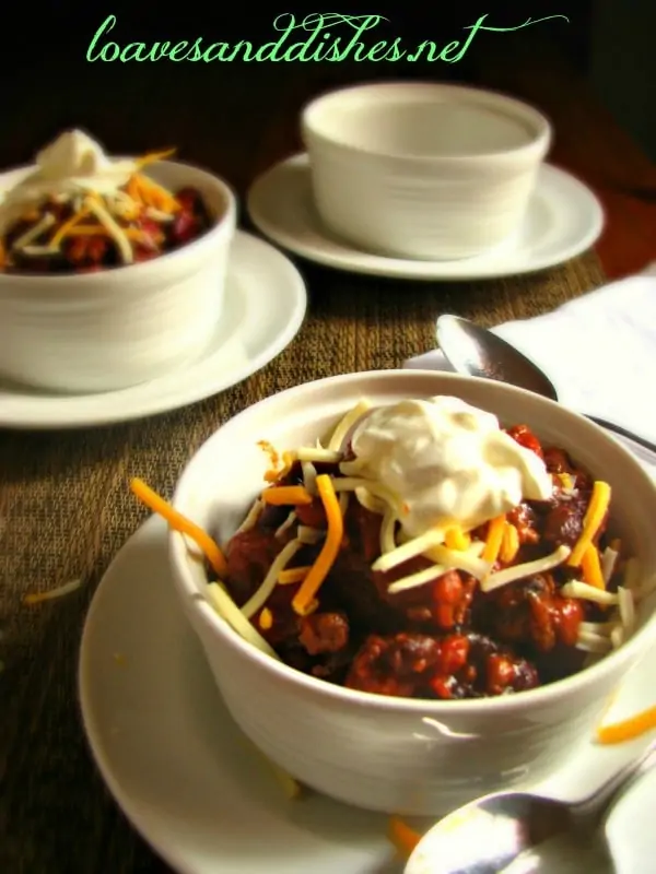 A closeup view of a small bowl of party chili with grated cheese and sour cream on top with other bowls in the background