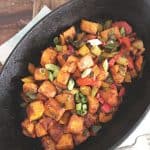 a black cast iron oval pan with sweet potato hash inside with wood in back ground