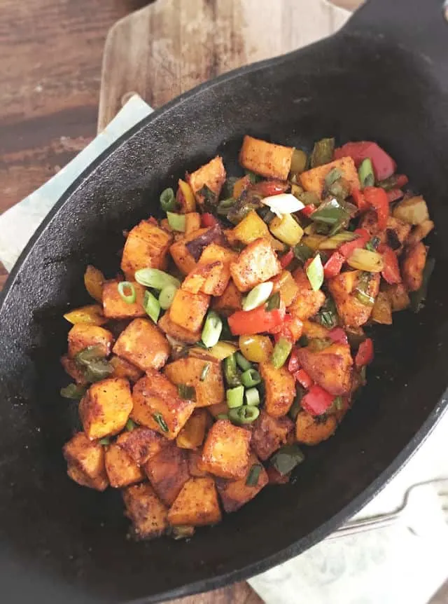 a black cast iron oval pan with sweet potato hash inside with wood in back ground