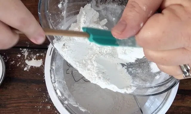 a photo of adding the dry ingredients to the mixer bowl with a green spatula