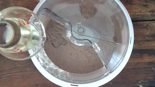 a wet measure pouring oil into the dry ingredients in the mixer bowl