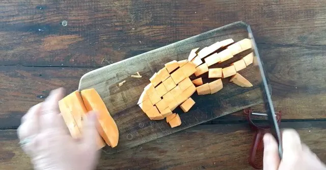 A sweet potato cut into 1 " cubes on a cutting board on wood table