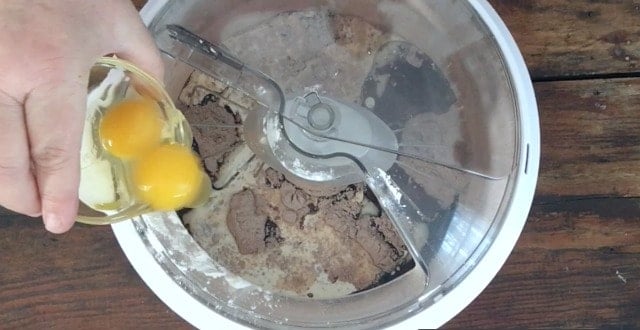 Two eggs being added to the mixer of the chocolate cake