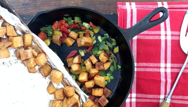 A photo of adding the roasted sweet potatoes to the frying pan of peppers and onions with red and white napkin in the background