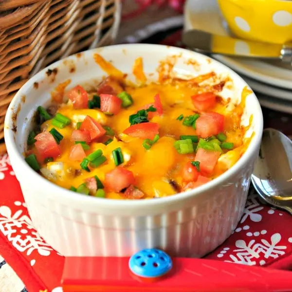white bowl of cheesy dish covered with tomatoes and scallions