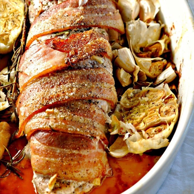 Close up photo of bacon wrapped pork loin in baking dish with garlic
