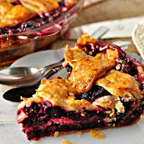 Slice Blackberry Pie Cobbler on a dish with spoons and pie in the background