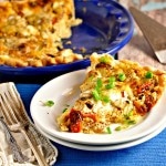 A slice fo Roasted Tomato and Garlic Quiche on a white plate with a blue placemat and two forks