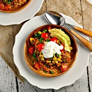 Southwest Corn Sauce in a wooden bowl with sour cream and avocado on top with two spoons on a white plate