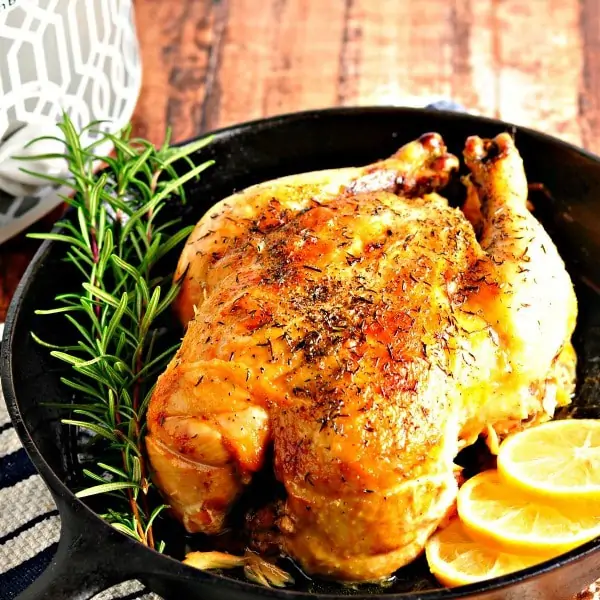roasted chicken in a cast iron pan with fresh rosemary and lemon slices
