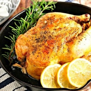 Roasted chicken in a cast iron skillet with fresh rosemary and lemon slices in the pan