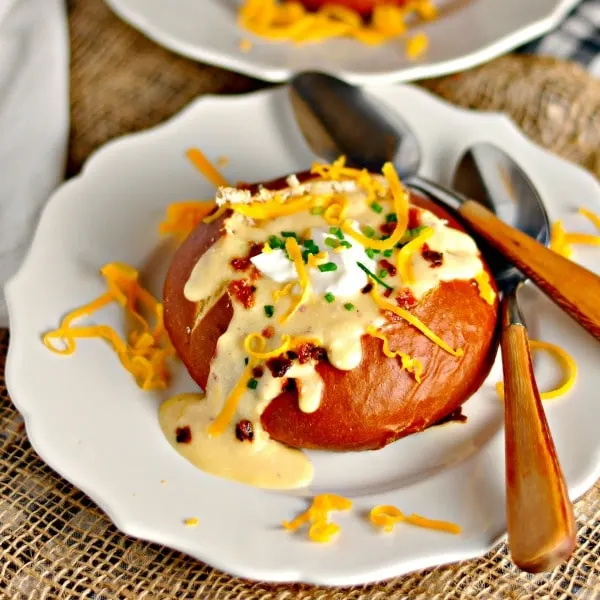 The Best Potato Cheese Soup in a bread bowl on a white plate with two spoons