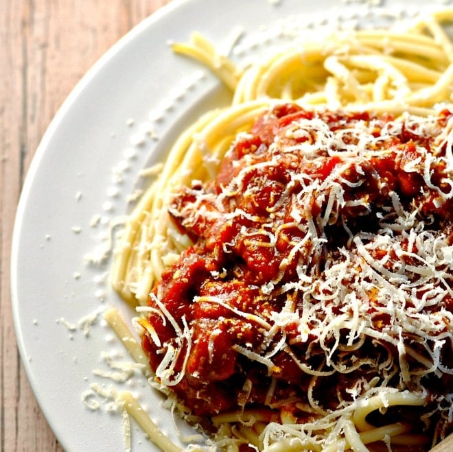 A white plate with spaghetti noodles and a thick red meat sauce on top