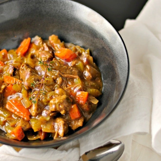 A close up photo of a black bowl full of classic beef stew showing how shiny the stew is.