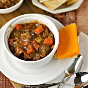 Classic Beef Stew in a white bowl with spoons and a cheddar cheese slice