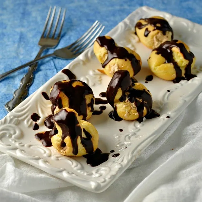 A long white plate with 6 Cream Puff with espresso Cream Filling and two forks