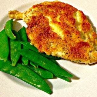 Chicken with breading and green snow peas on a white plate