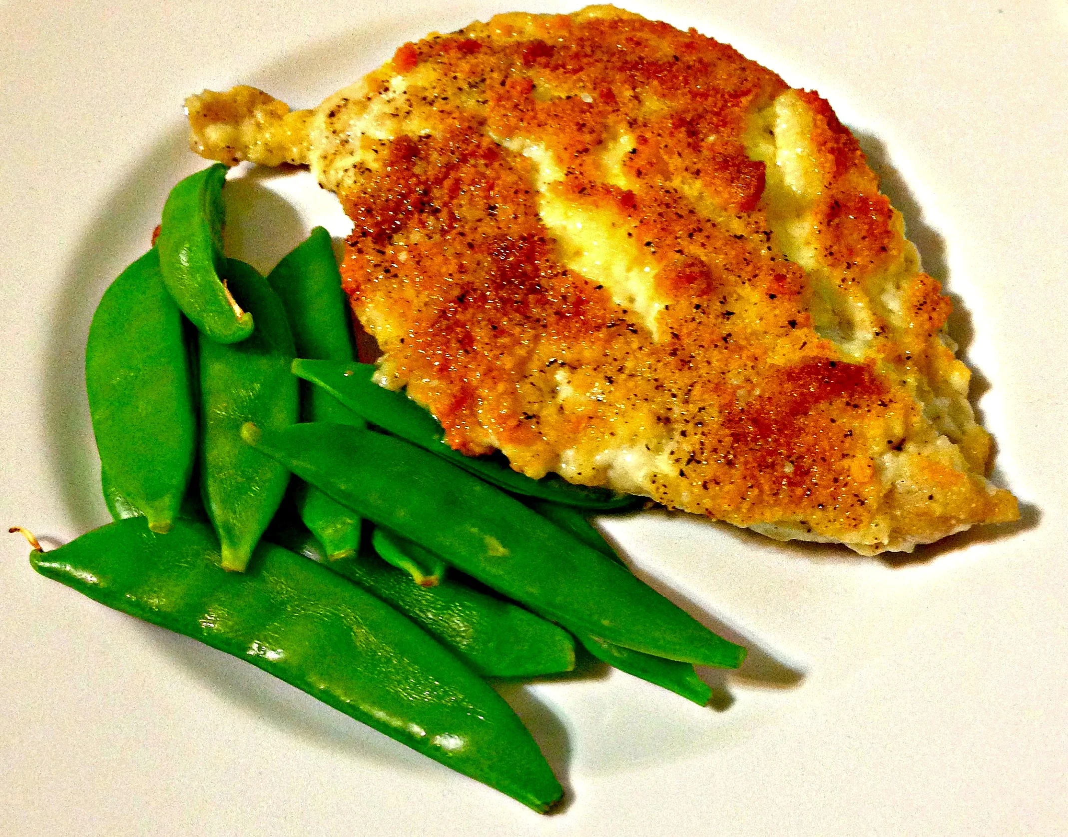 Chicken with breading and green snow peas on a white plate