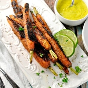 Vindaloo Curry Spiced Carrots on a white dish with slices of lime and fresh parsley on the side