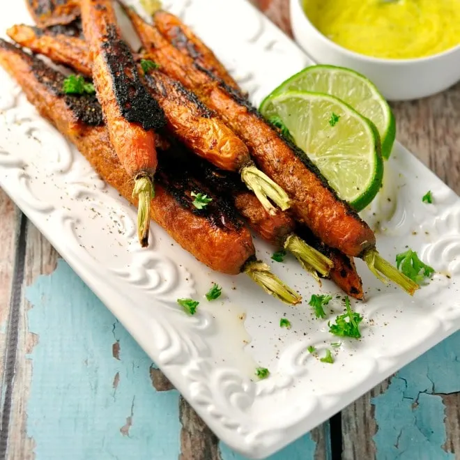 Vindaloo Curry Spiced Carrots on a white dish with sauce and lime slices