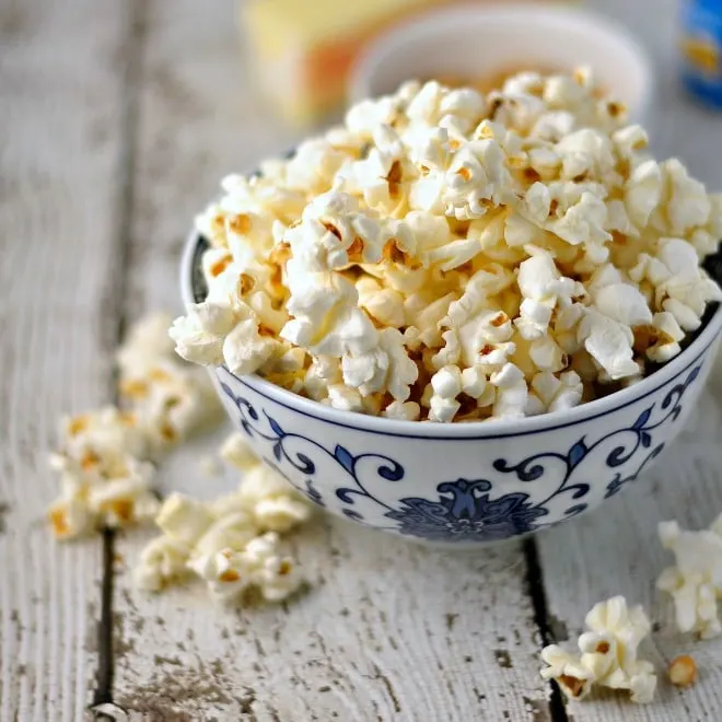 Blue flowered bowl holding too much popcorn with some spilling over onto the white wooden counter