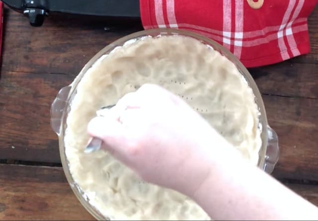 hand using a fork to poke holes in the crust of the strawberry pie with jello