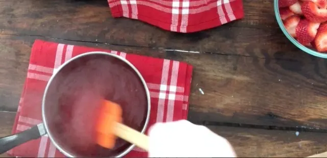 hand stirring an orange spatula in the strawberry pie glaze