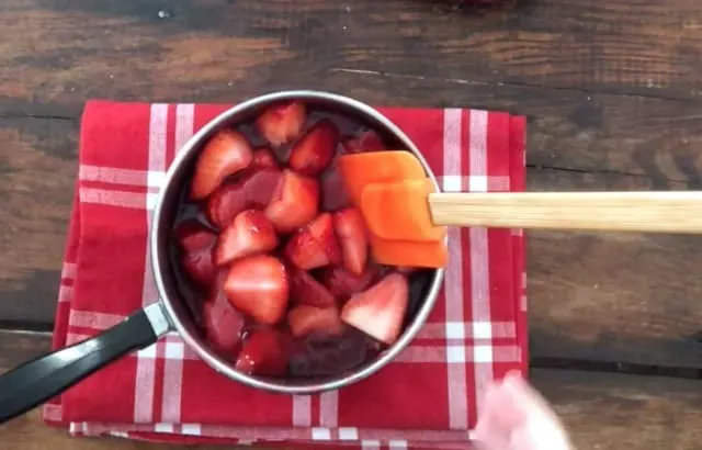 Fresh strawberries added to the strawberry pie with jello in sauce pan with red napkin