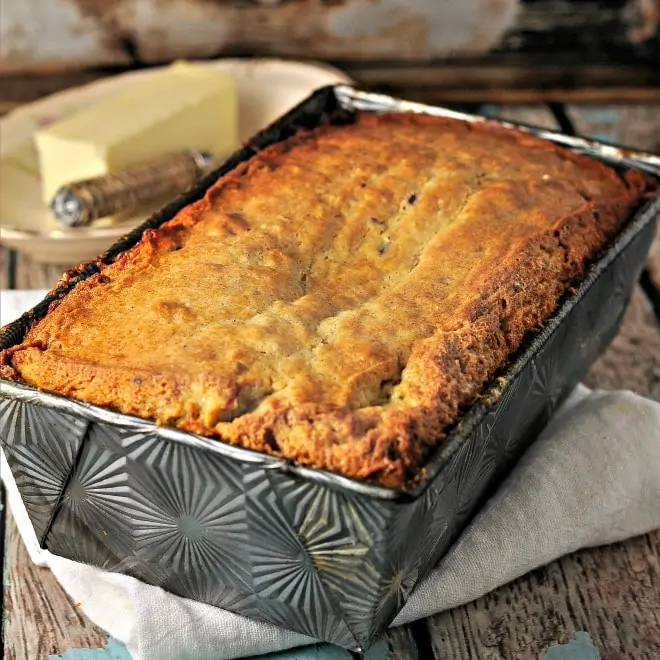 banana nut bread in a silver pan sitting on white napkin, butter in back ground