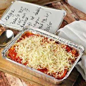 Easy Gift Lasagna in an aluminum tin on a cutting board with a spoon and a white napkin