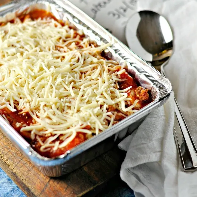 Uncooked lasagna in an aluminum baking tin with a spoon