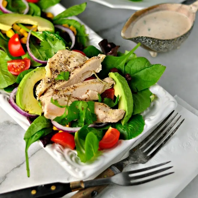 southwest chiptole chicken salad with chicken and avocados on a white plate with two forks and a small bowl of dressing