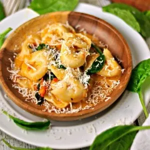 Spinach Cheese Tortellini in a bowl on a white plate with fresh basil sprinkled around the plate