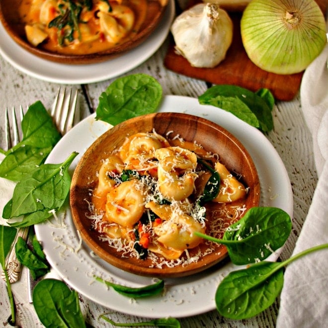 Spinach Cheese Tortellini on a plate with fresh basil and two forks on a wooden table