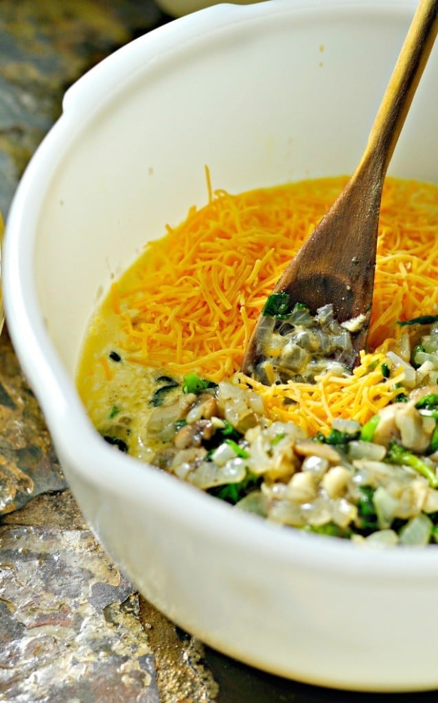 Cheese, sautéed vegetables in a white bowl with a wooden spoon