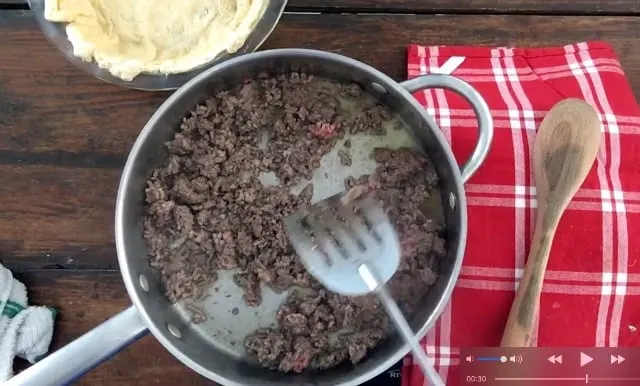 Ground beef in a frying pan with a red napkin and wooden spoon
